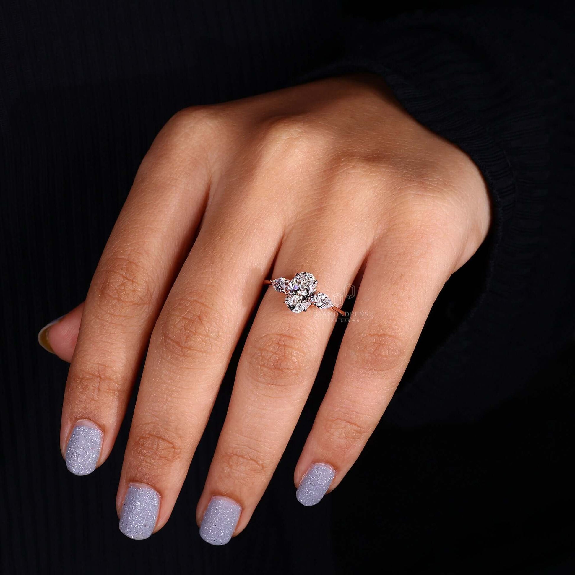 Oval diamond engagement ring with pear side stones on a model's hand